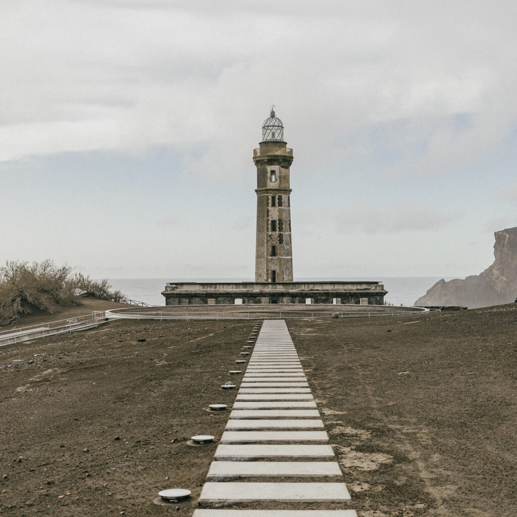 The iconic Capelinhos Lighthouse standing amidst the volcanic landscape of Faial Island, a historical landmark shaped by the 1957 eruption.