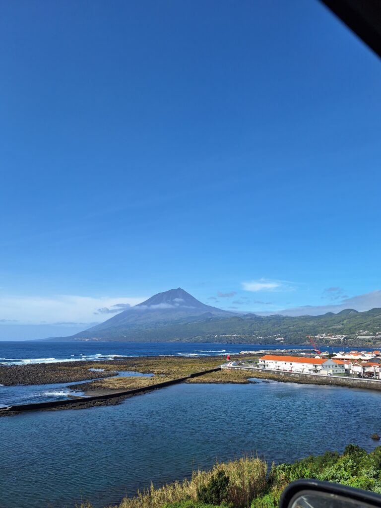 A scenic view of Mount Pico, Portugal’s highest peak, seen from across the blue ocean, with a charming coastal town in the foreground.