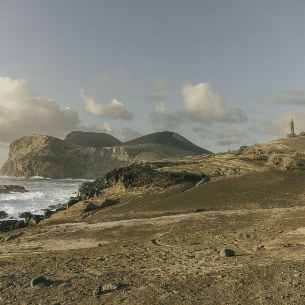 The surreal volcanic landscape of Capelinhos, Faial, with the iconic lighthouse standing on the barren terrain.