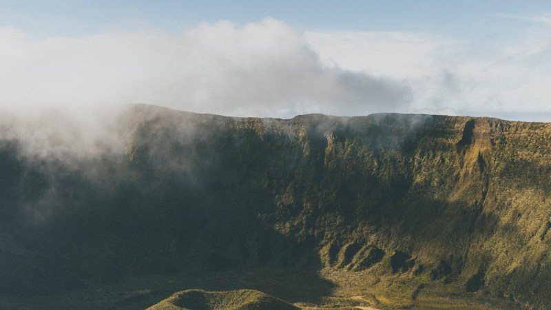 A grassy volcanic crater under a clear blue sky with scattered clouds.