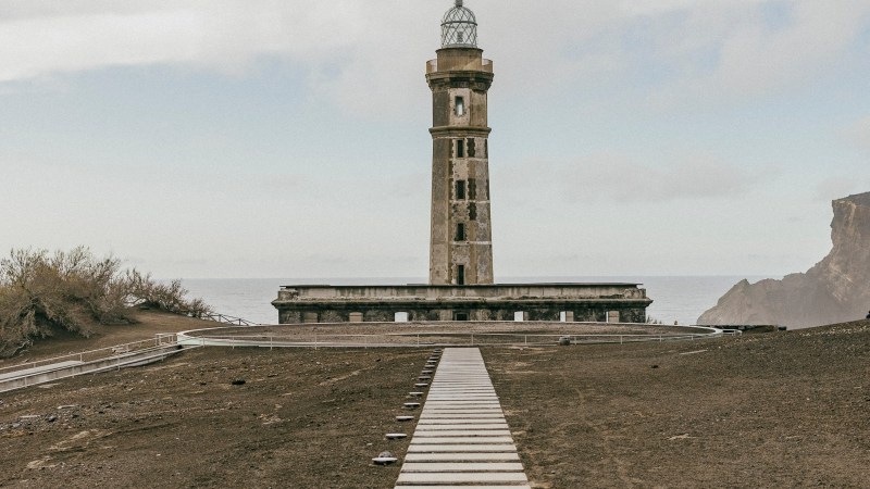 Lighthouse on a coastal landscape with a stone pathway leading to it.