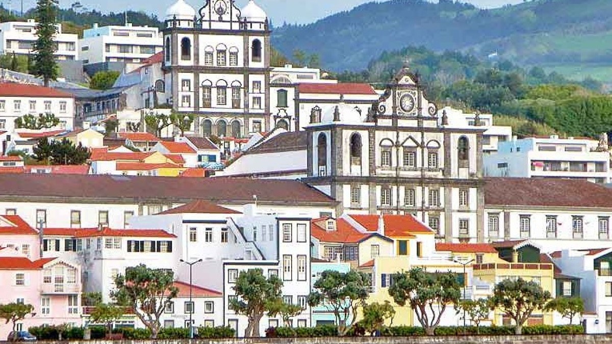 Coastal townscape with colorful buildings, churches, and lush hills in the background.
