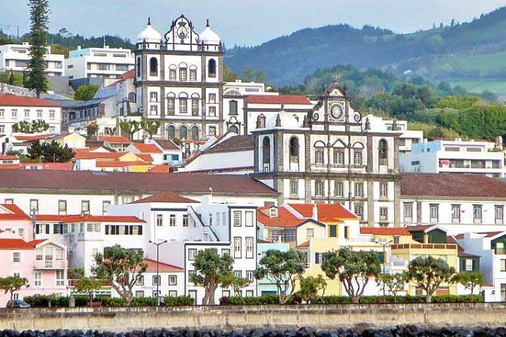 Coastal townscape with colorful buildings, churches, and lush hills in the background.