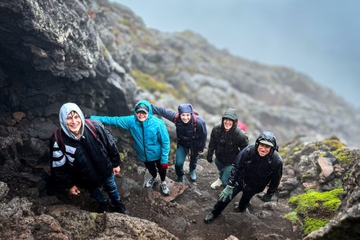 Five people in jackets hiking on rocky terrain, smiling at the camera.