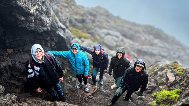 Five people in jackets hiking on rocky terrain, smiling at the camera.