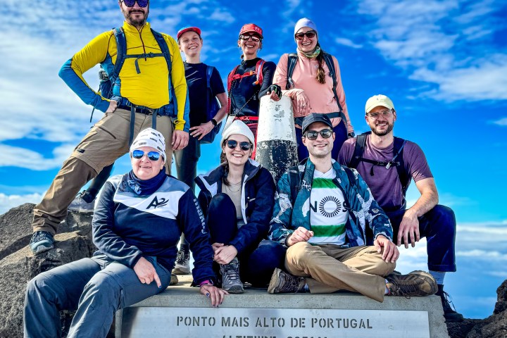 Group of hikers smiling at Portugal's highest point, altitude 2351m, with a clear blue sky.