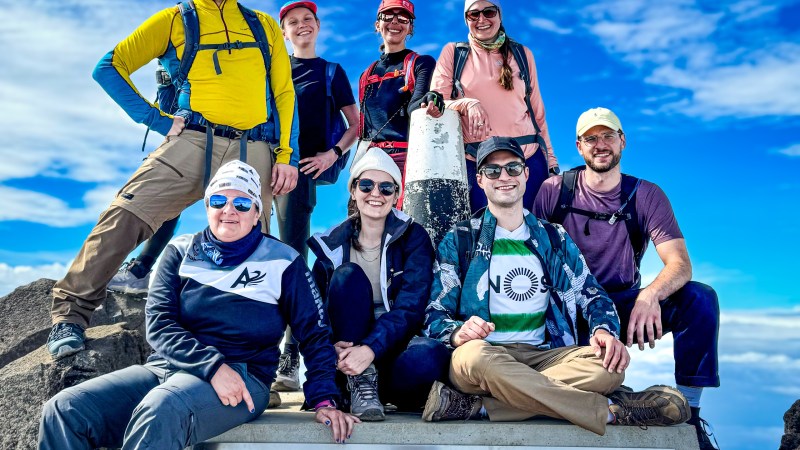 Group of hikers smiling at Portugal's highest point, altitude 2351m, with a clear blue sky.