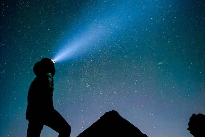 Silhouette of person with headlamp against starry night sky, standing on hill.