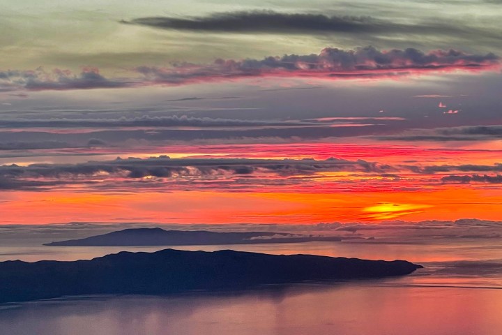 Colorful sunset over mountains and sea with vibrant clouds and reflections.