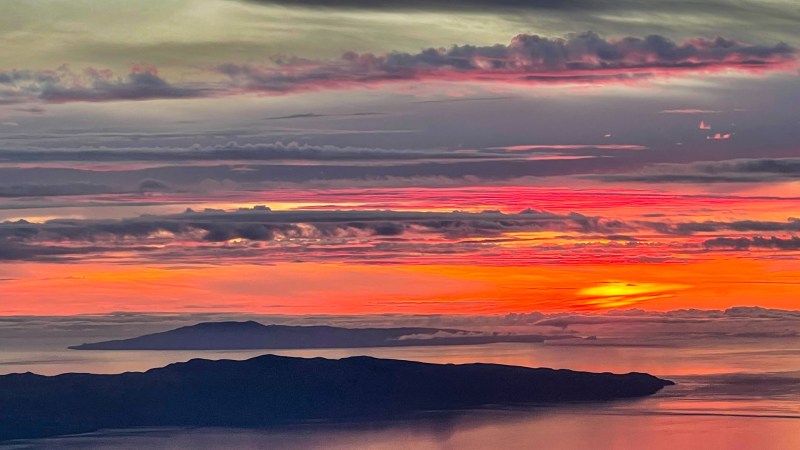 Colorful sunset over mountains and sea with vibrant clouds and reflections.