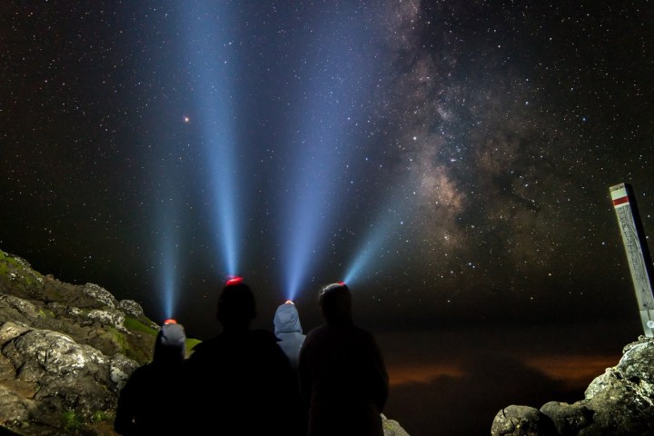 Three people with headlamps under a starry sky, beams pointing upwards towards the Milky Way.