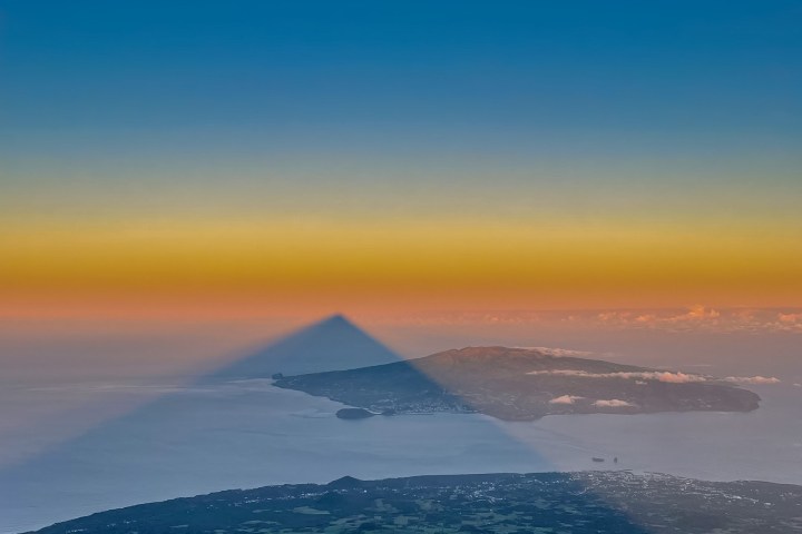 Triangle shadow over landscape, colorful sky, and distant moon.