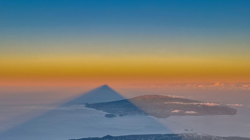 Triangle shadow over landscape, colorful sky, and distant moon.