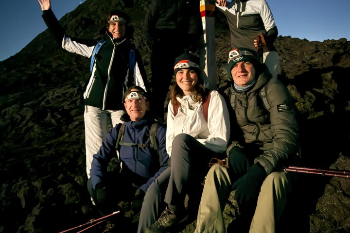 Group of six hikers with headlamps posing on a rocky mountain at night.