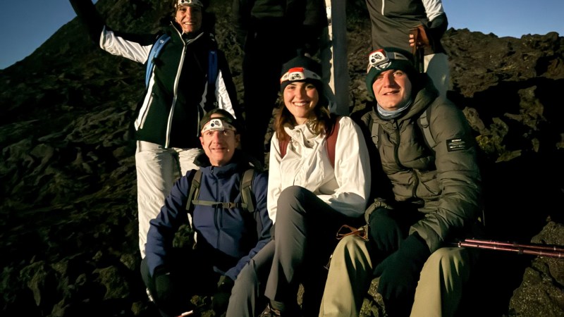 Group of six hikers with headlamps posing on a rocky mountain at night.
