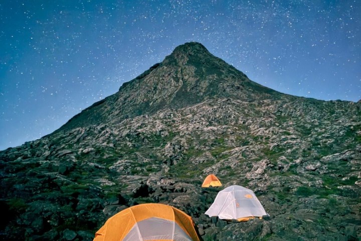 Night scene with tents on rocky terrain beneath a starry sky and mountain.