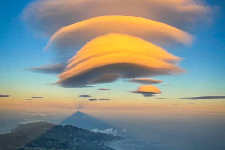 Sunset over ocean with layered clouds and shadowed mountain landscape.