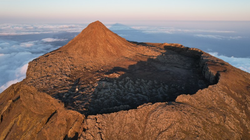 Aerial view of a volcanic mountain peak with a crater, surrounded by clouds.