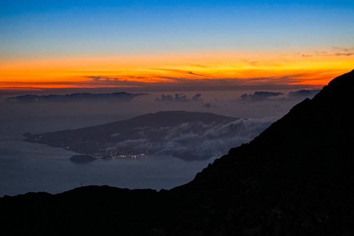 Silhouette of a mountain at sunset with colorful horizon and distant island.