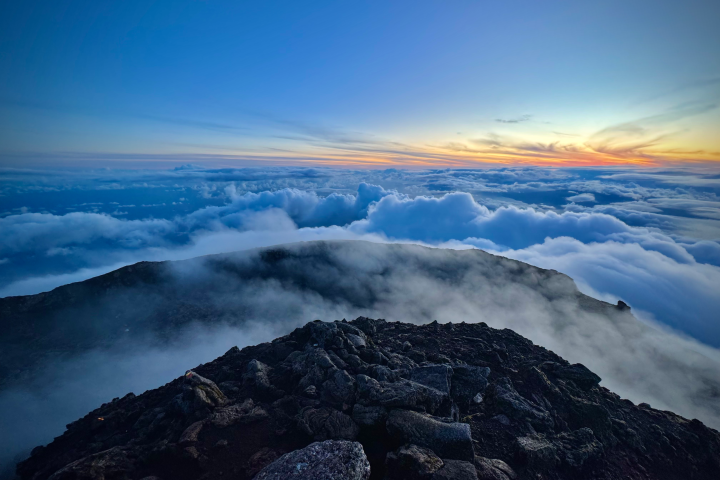 Rocky mountain peak above clouds at sunset, blue sky and horizon.