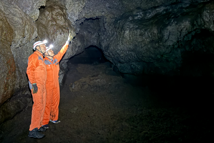 Two people in orange suits and helmets exploring a cave.