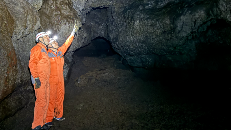 Two people in orange suits and helmets exploring a cave.