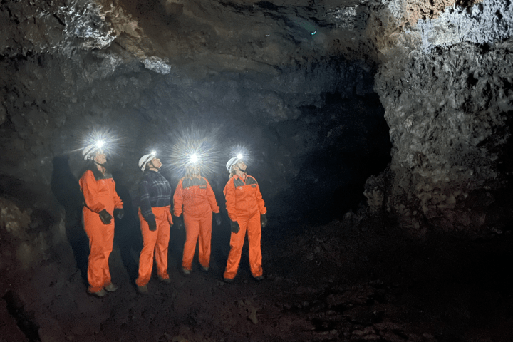 Four people in orange suits with headlamps exploring a cave.