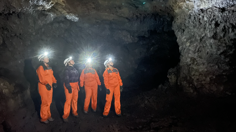 Four people in orange suits with headlamps exploring a cave.