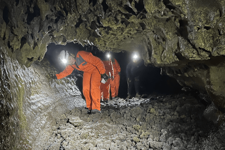 People in orange suits and helmets exploring a rocky cave with headlamps.