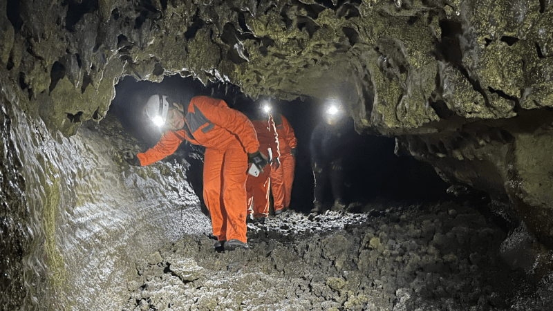 People in orange suits and helmets exploring a rocky cave with headlamps.