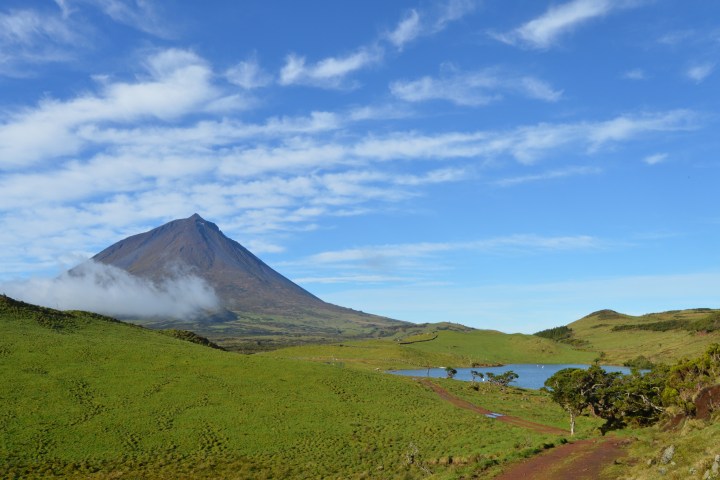 Mountain peak with cloudy sky, grassy hills, and a small lake in the foreground.