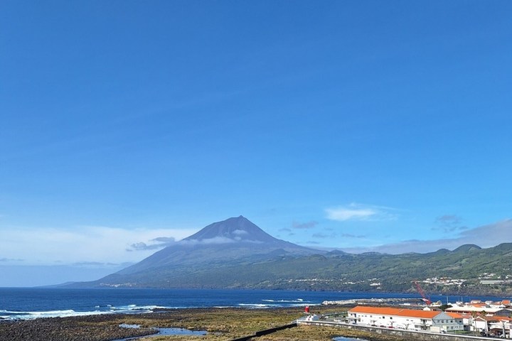 A distant mountain with buildings by the ocean under a clear blue sky.
