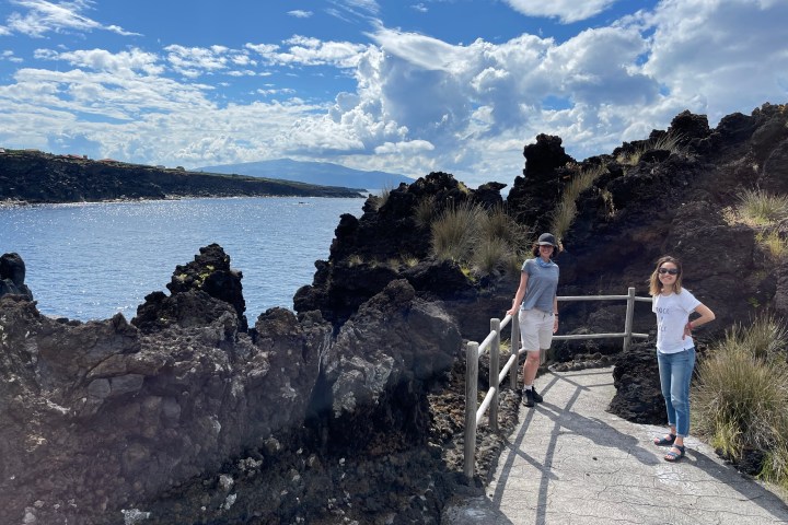 Two people on a rocky path by a body of water with a cloudy sky.