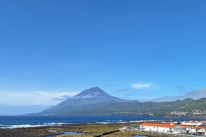 Coastal view with a mountain and small town under clear blue sky.