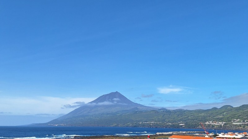 Coastal view with a mountain and small town under clear blue sky.