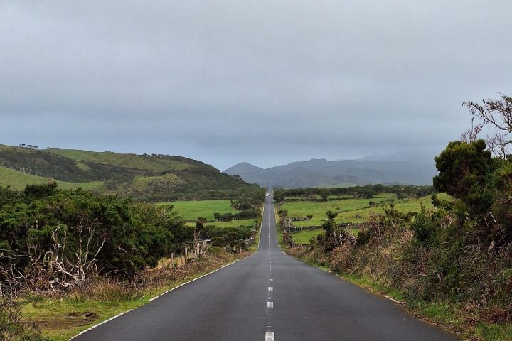 Long straight road through green landscape under cloudy sky.