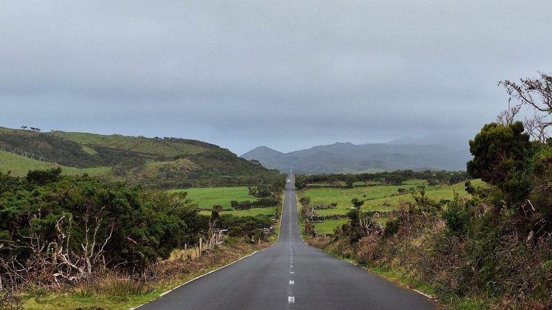 Long straight road through green landscape under cloudy sky.