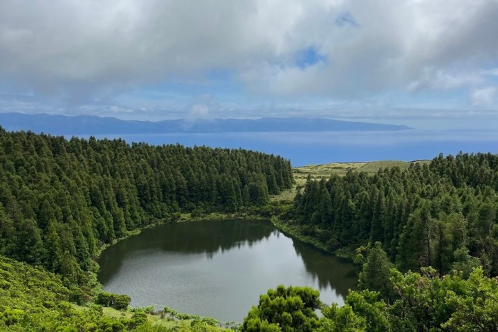 Scenic view of circular lake surrounded by dense forest under cloudy sky.