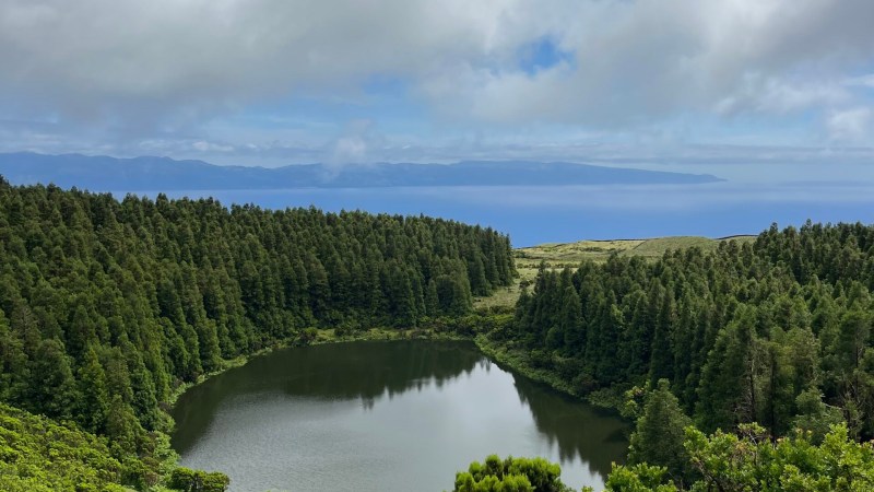 Aerial view of a forested lake surrounded by lush greenery under a cloudy sky.