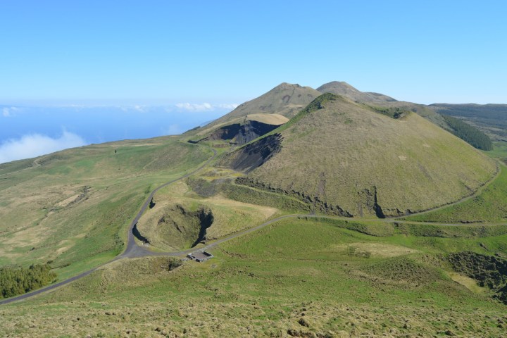 Green hills with winding road under clear blue sky and distant ocean view.
