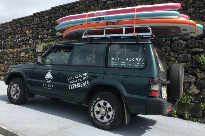 SUV parked by stone wall with surfboards on roof rack.