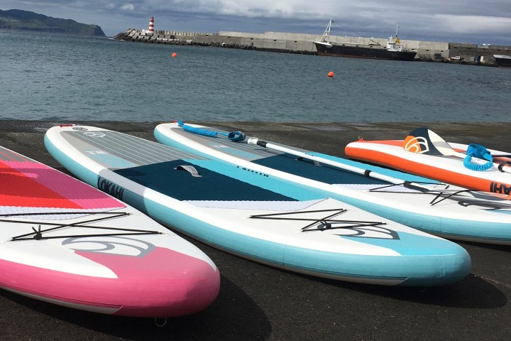 Colorful paddleboards on a concrete surface by the sea, lighthouse and boats in background.