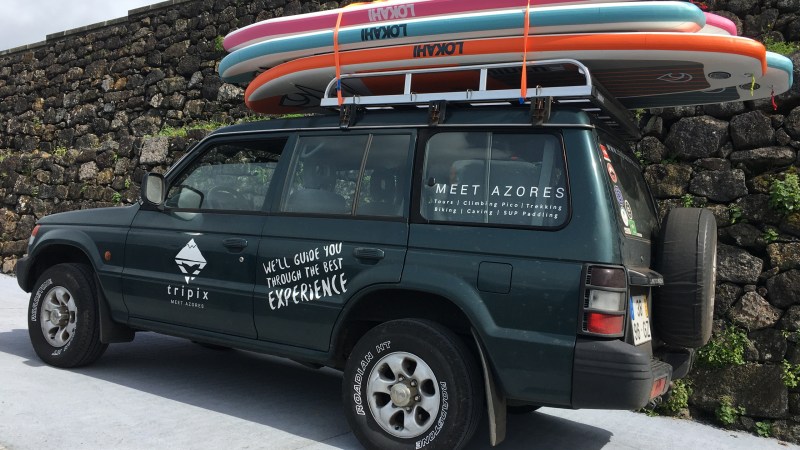 SUV with surfboards on top parked by a stone wall.