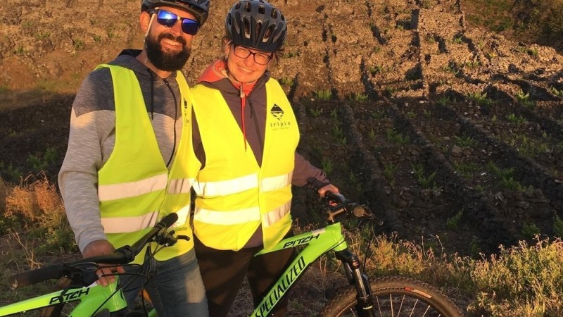 Two cyclists in yellow vests pose with bikes in front of a mountain.