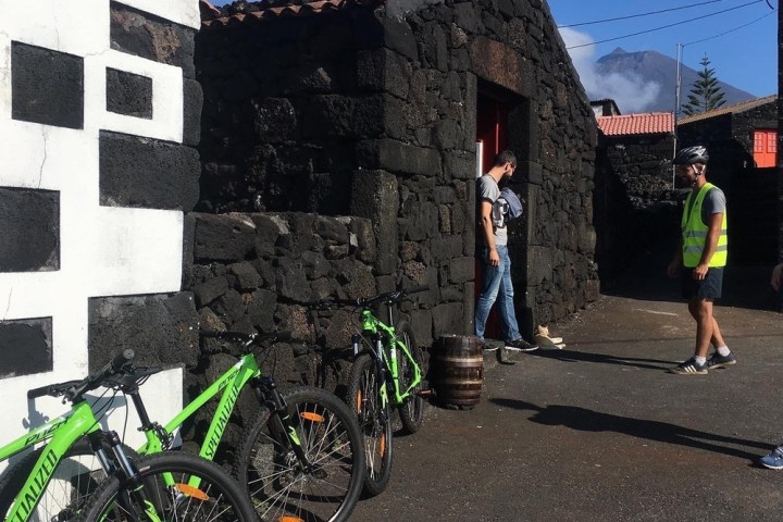 Three green bikes and two people by a stone building with mountain in background.