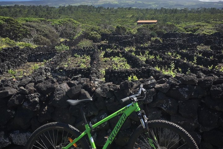 Green bike by stone wall with distant mountain under cloudy sky.