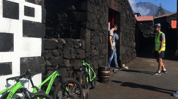 People with bikes near stone building, one wearing yellow vest under clear blue sky.