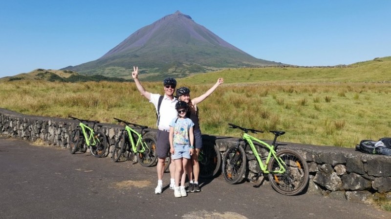 Family with bicycles poses in front of a mountain on a sunny day.