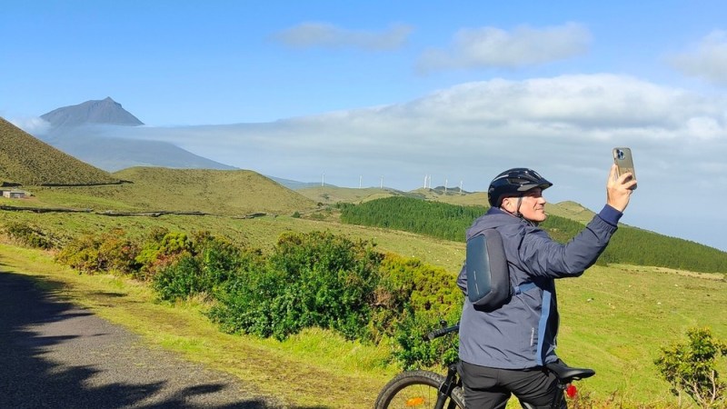 Cyclist taking a selfie with a scenic mountain view and clear blue sky.