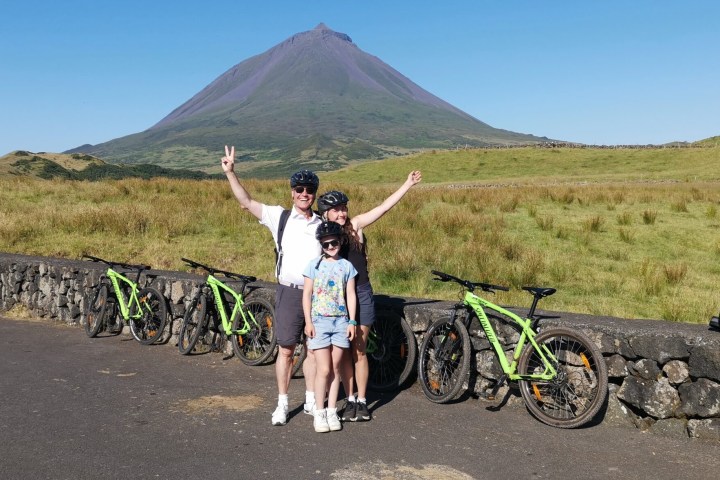 Family with helmets and bikes, posing in front of a mountain in a grassy landscape.